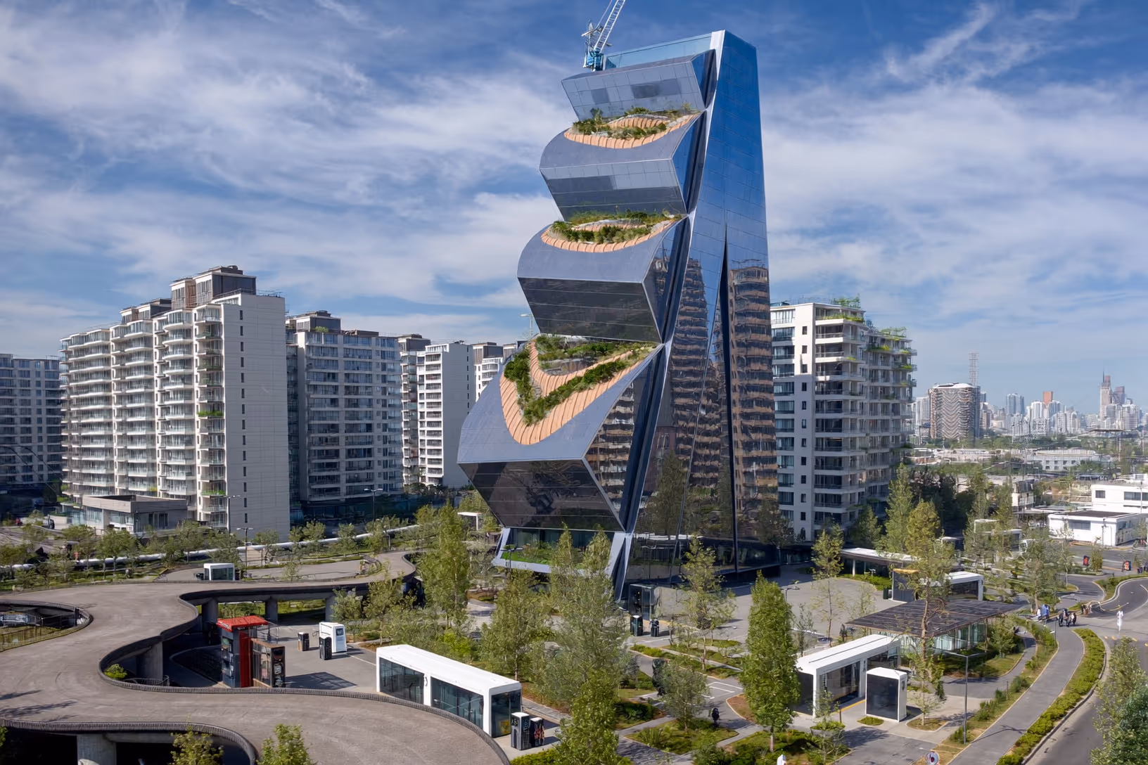 Tour à façade miroir sombre découpée en segments horizontaux décalés, avec des terrasses densément végétalisées entre chaque décrochement, dans un contexte urbain dense sous un ciel bleu.