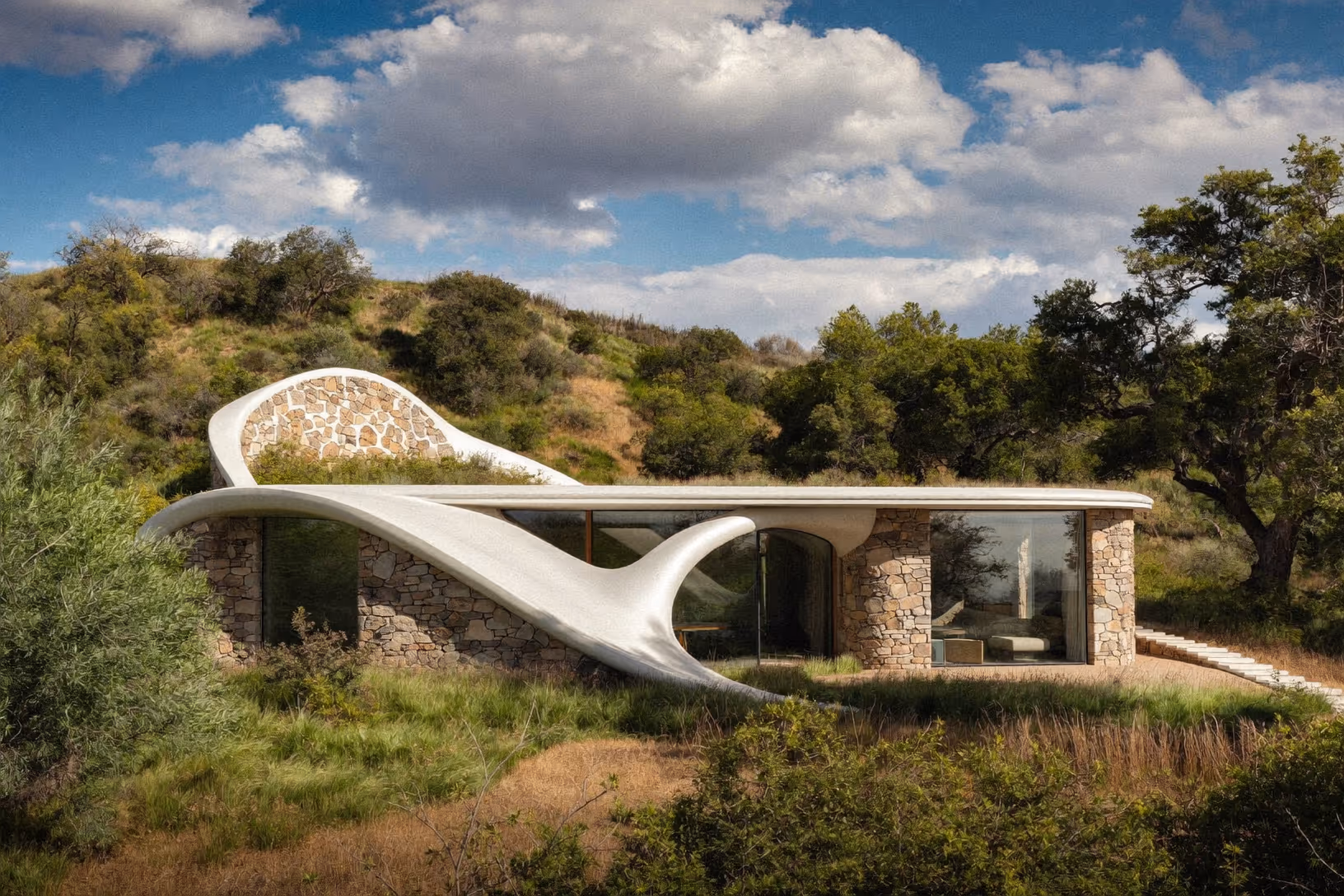 Maison basse à murs de pierre sèche surmontée d'une toiture courbe en béton blanc aux formes organiques, insérée dans un paysage de garrigue et de collines boisées sous ciel nuageux.