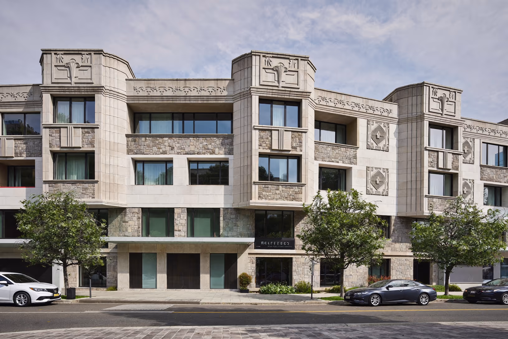 Immeuble urbain de quatre niveaux en pierre calcaire claire et pierre de taille grise, orné de frises et médaillons Art déco, menuiseries sombres, arbres alignés en pied de façade.