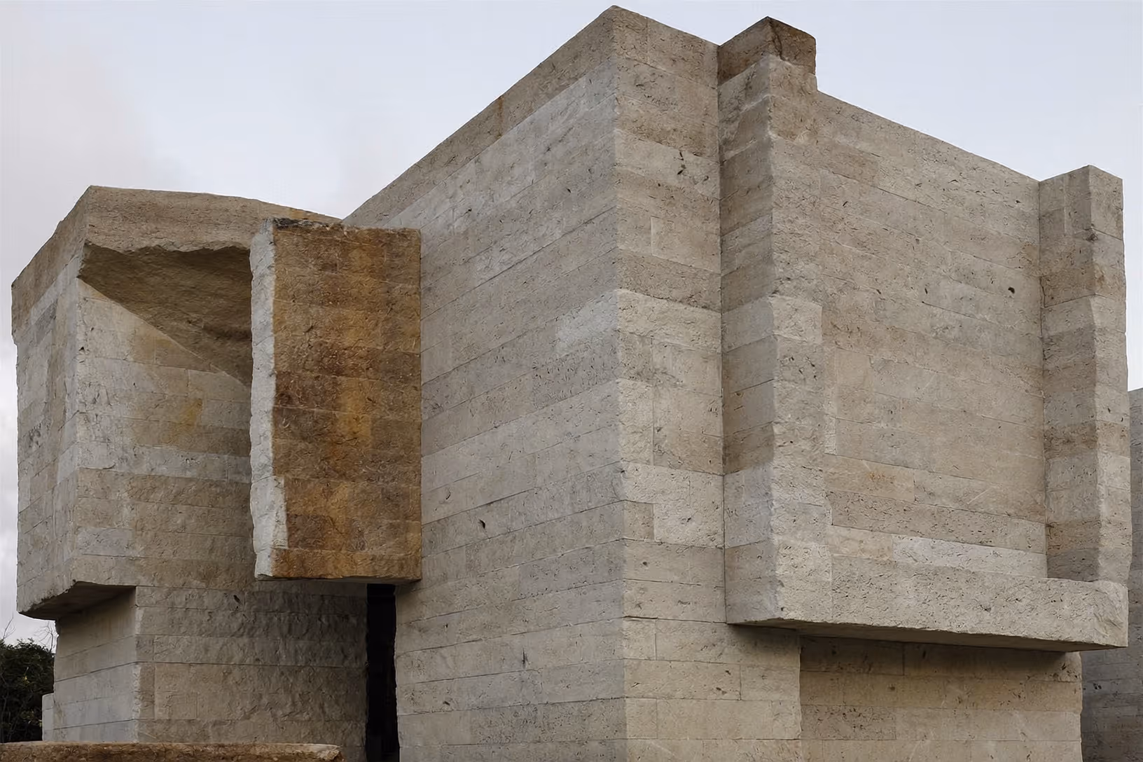 Façade d'une maison entièrement construite en blocs de pierre calcaire appareillés, composée de volumes cubiques décalés avec une loggia profonde creusée dans le mur gauche.