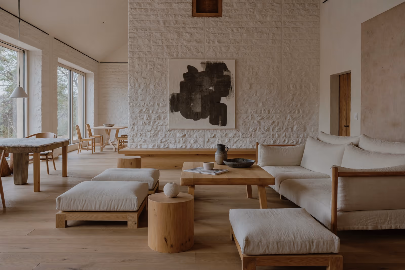 Salon Japandi lumineux : mur de pierre blanche, art abstrait, banquettes basses en bois et lin.