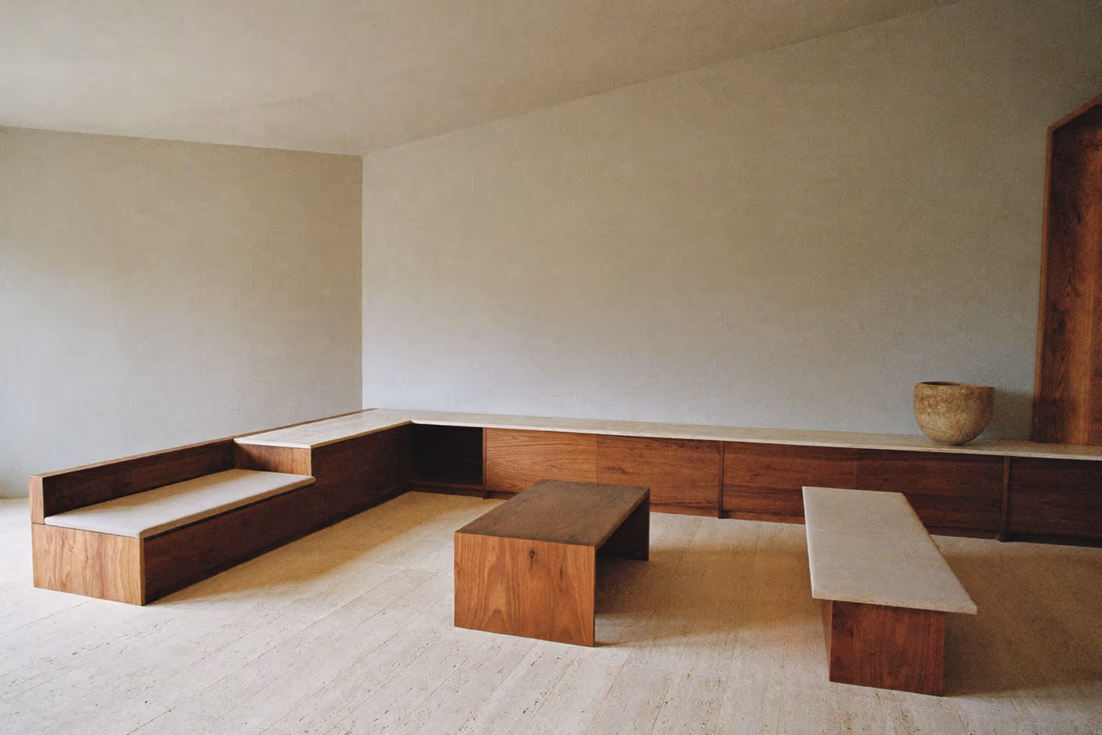 Pièce épurée aux banquettes basses en bois disposées le long des murs, esthétique de l'espace vide.