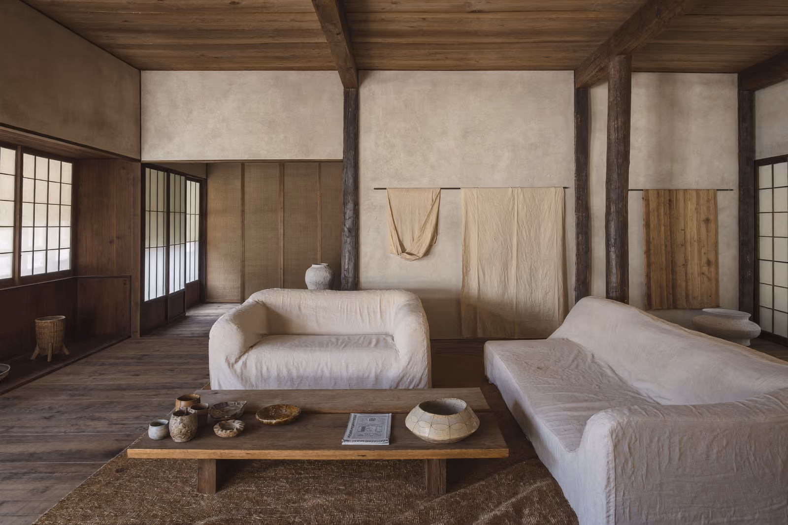 Pièce de style tatami à cloisons shoji, canapés blancs et table basse en bois garnie de céramiques.